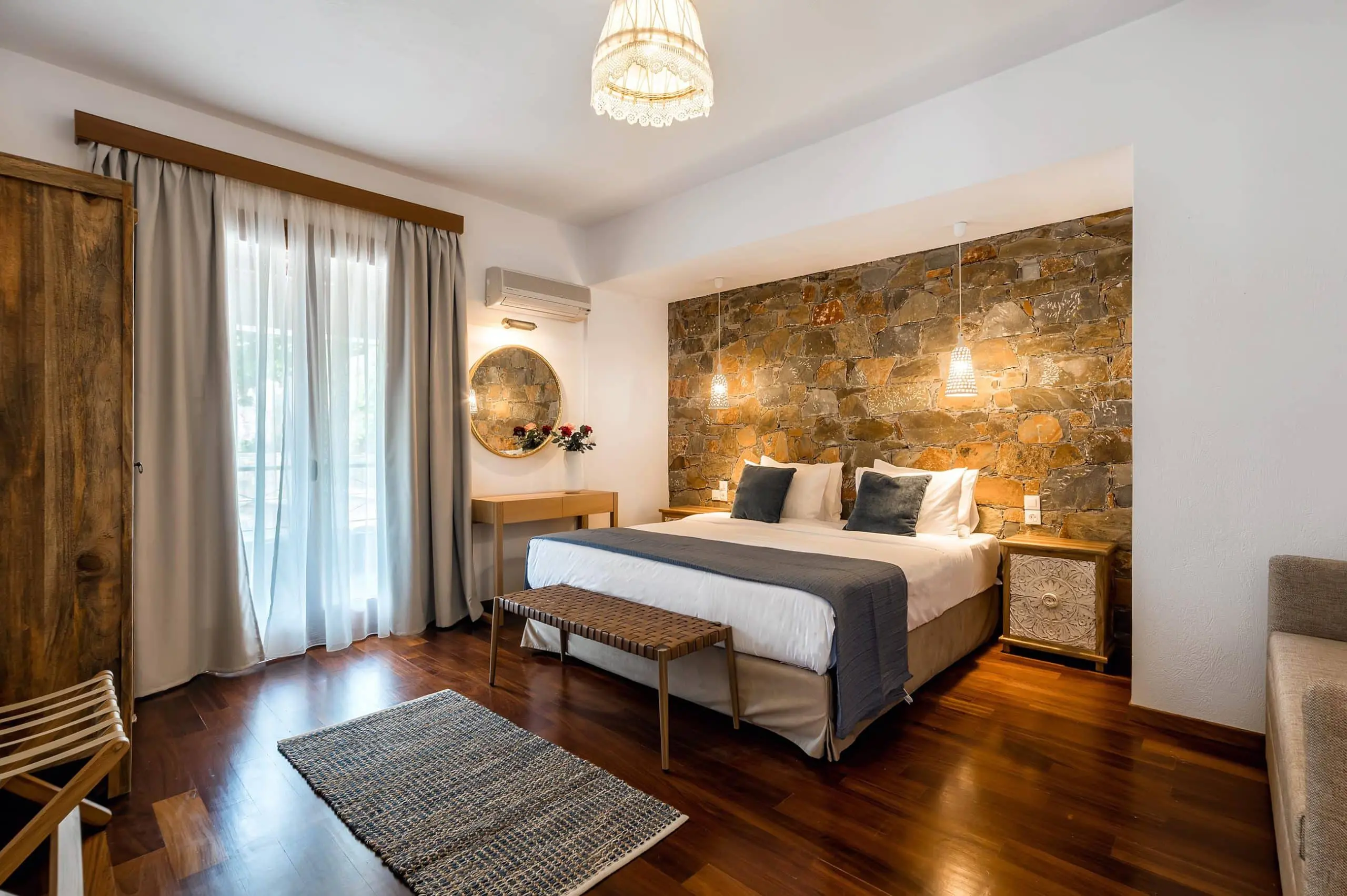 Cozy, elegantly designed room with a king-sized bed, warm wooden flooring, a stone accent wall, and soft lighting that creates a welcoming atmosphere.
